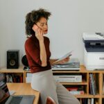 A woman sitting at a desk having a call next to a Xerox® C325 Printer